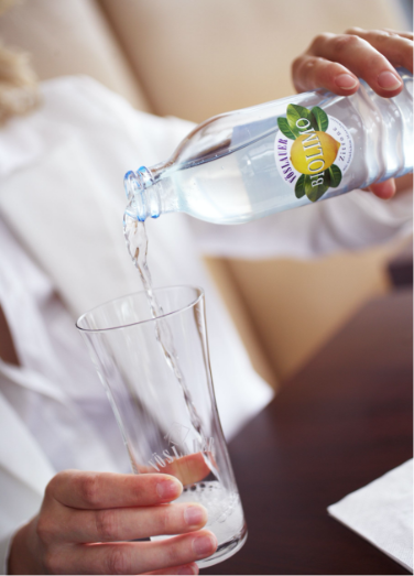 Eine Person schenkt in eine Vöslauer Glas eine Vöslauer Biolimonade Zitrone ein