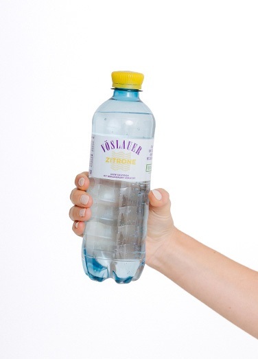 Eine Hand hält eine Vöslauer Flavours Zitrone Flasche