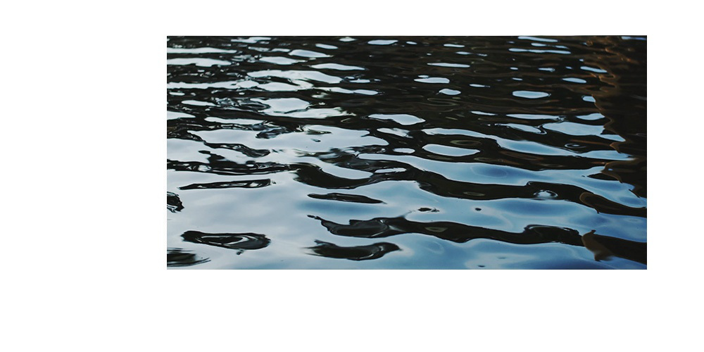 Dunkles leicht welliges Wasser, man sieht die Spiegelung eines Himmels